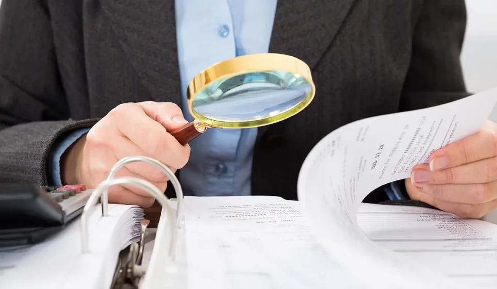 What Happens If You Get Audited and Fail? Audit Penalties and Other Consequences 1 man looking over tax documents with a magnifying glass.