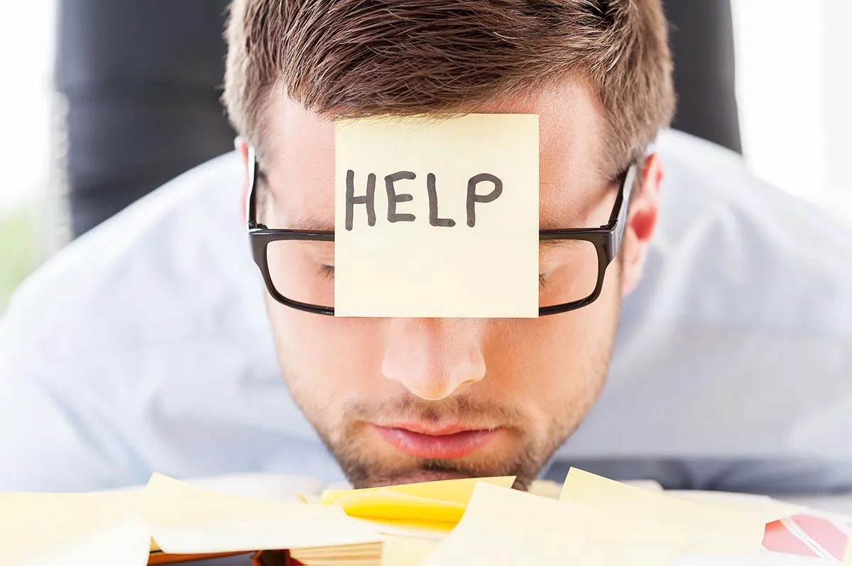 Man Resting Head on Tax Audit Paperwork with Help Sticky Note on Forehead